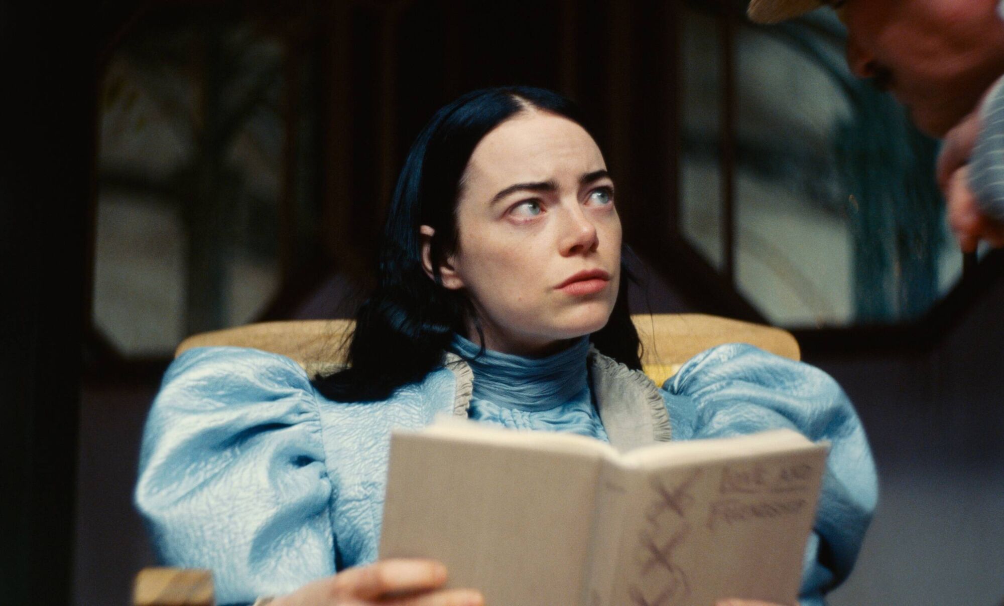 Emma Stone in the movie Poor Things looking up from a book